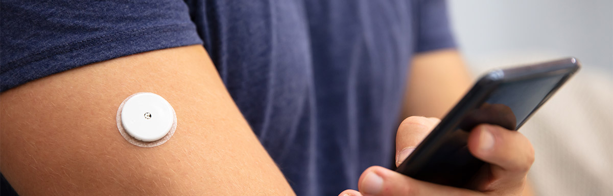 Frauenhand sticht mit einem klassischen Blutzuckermessgerät in die Fingerkuppe des Zeigefingers, um eine kleine Blutprobe zu gewinnen.
