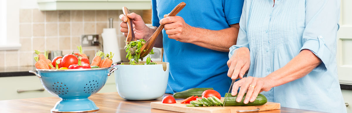 Diabetes und Ernährung: Ein älteres Paar steht in der Küche und bereitet einen Salat zu