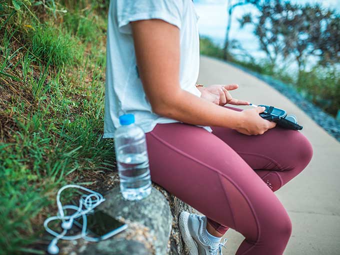 Junge Frau sitzt im Sportoutfit und mit Wasserflasche im Freien - Bewegung bei Diabetes hilft, die Krankheit in den Griff zu bekommen.