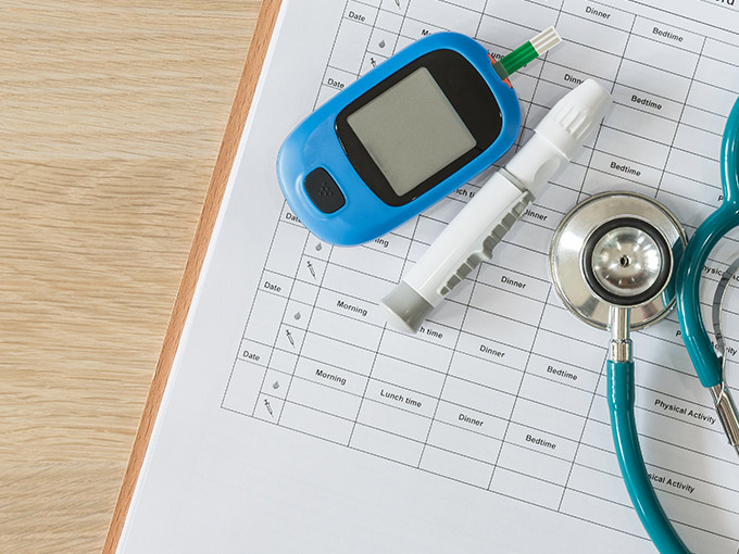 Ärztliche Überwachungs des Blutzuckerspiegels: Auf einem noch leeren Diabetes-Tagebuch liegen Blutmessgerät, Lanzette und blaues Stethoskop.